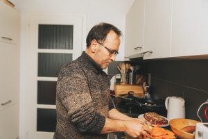 Middle age man cooking dinner in the kitchen, peeling off potato with peeler