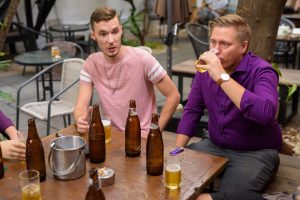 Group of men outdoors sitting and talking while drinking beer