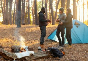 Back view of three friends camping in autumn forest, planning next trip, free space