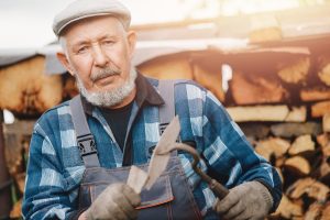 Senior smiling man is sharpening tool for cultivating farm soil. Agriculture concept