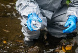 hands scientist, in a protective suit and gloves, holding a tube of water for the sample