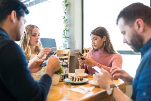 Distracted male and female friends using smartphones while sitting together at restaurant