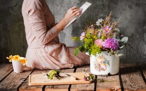 female artist draws a composition of wild flowers in a pot in a rustic style, a sketchbook on a table with pencils. Sketch art, artist inspiration, design, hobby, drawing school. hands close up