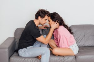 Side view of handsome man touching face of beautiful girlfriend on couch on gray background