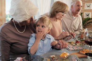 Grandmother sitting at dinner table with her grandson and feeding him at home