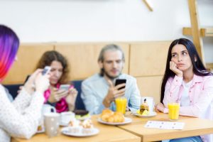 Young people guys and girls are having meeting, sitting at table in cafe. Friends are holding smartphones and browsing social networks instead of speaking. Addiction to gadgets, internet concept.