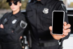 Smartphone with blank screen in hand of police officer near colleague on blurred background