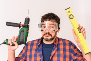 DIY enthusiast man holds a drill. White background. Plain shirt.
