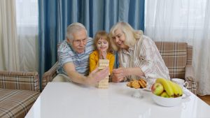 Excited child girl kid involved in build blocks board game with senior grandmother and grandfather