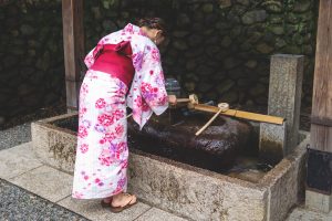 Kyoto, Japan - September 15, 2017: Woman in kimono rinsing hands at Japanese purify water fountain, called chozubachi, at Fushimi Inari Taisha shrine