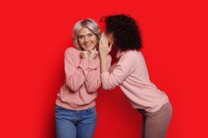Red background. Sisters gossiping. Whispering at the ear a secret.