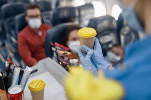 Close up shot of hands in protective gloves of flight attendant serving drinks to passengers on board. Traveling by airplane during Covid19 pandemic
