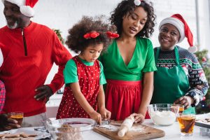 african american women and girl preparing christmas cookies near granddad standing with hand on hip