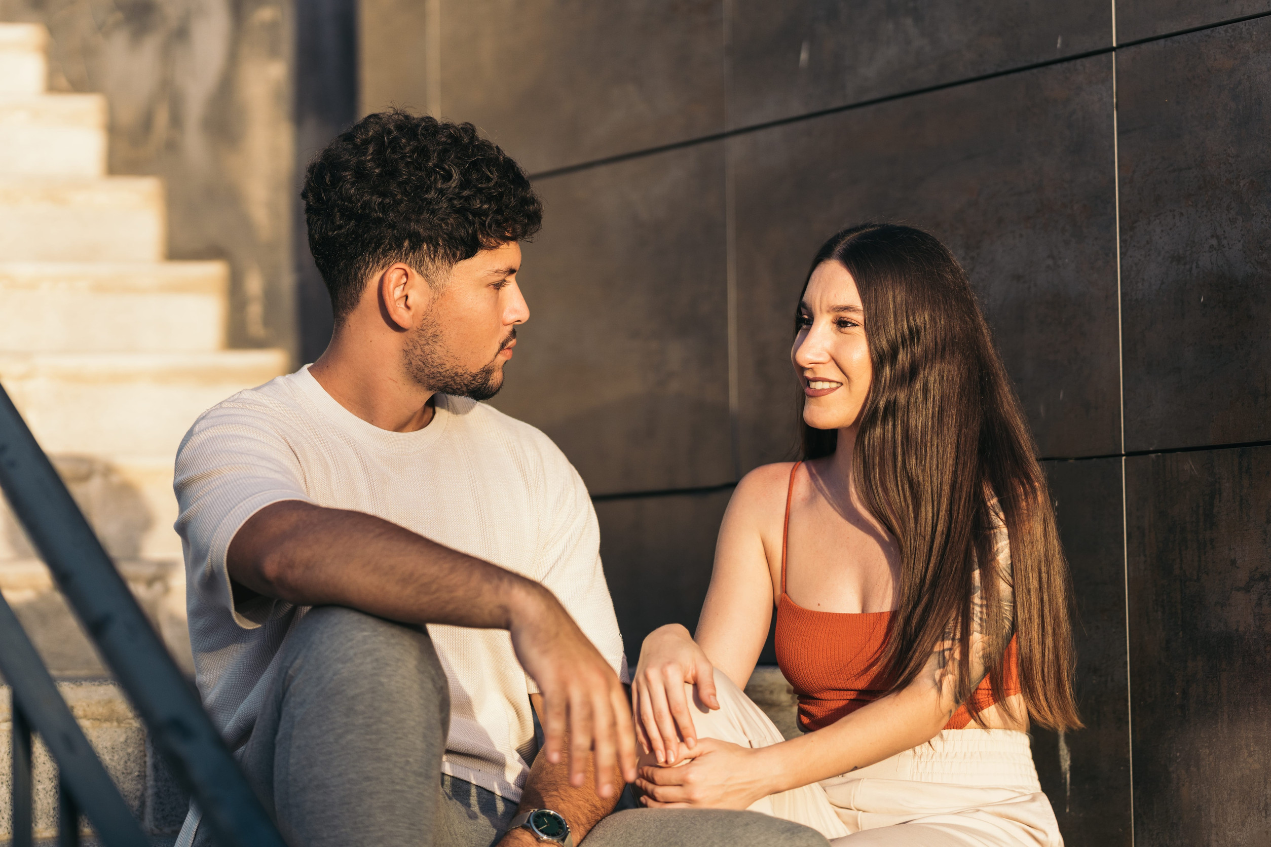 Young couple sitting on outdoor stairs talking during sunset