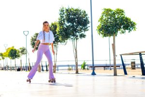 Portrait of beautiful blonde teenager girl with cool pigtails , white t-shirt and flared pink pants skating on rollers in park