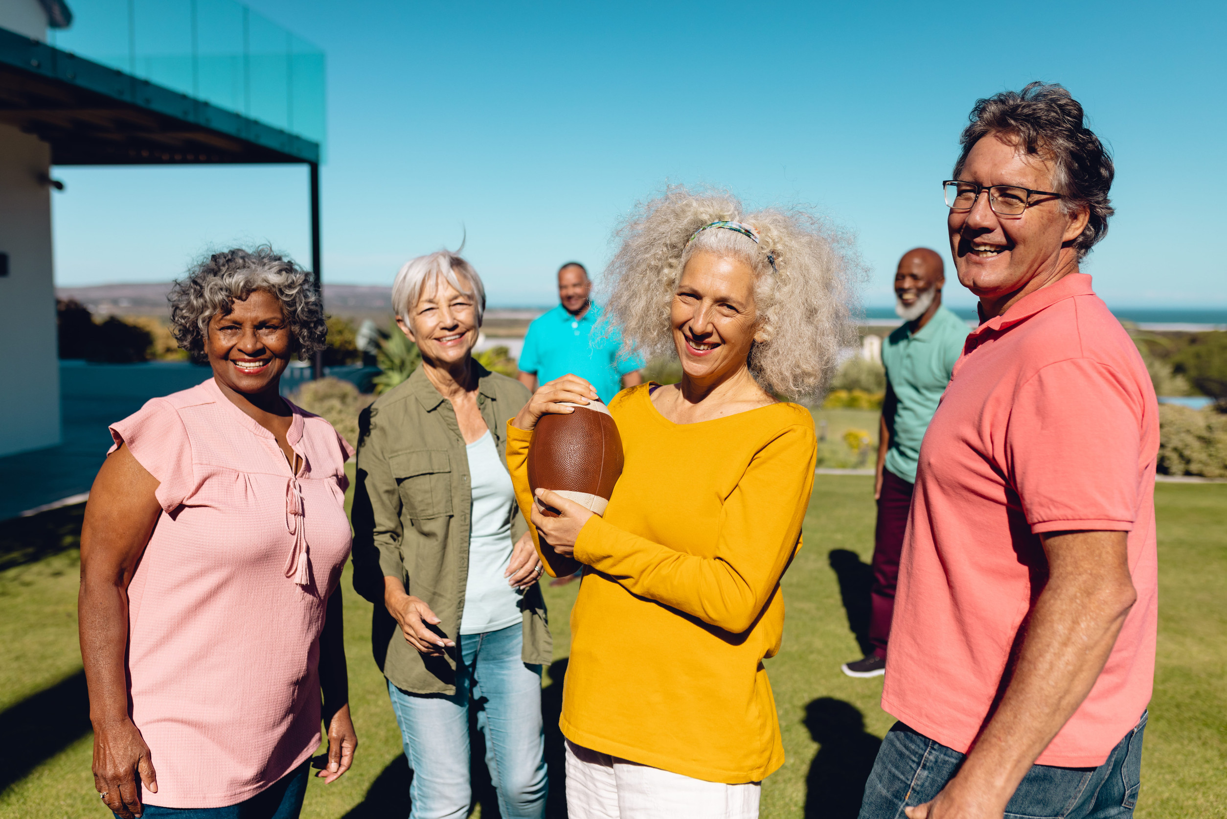 Portrait of happy multiracial senior friends playing rugby in yard against clear sky at nursing home. Summer, unaltered, sport, togetherness, enjoyment, support, assisted living, retirement concept.