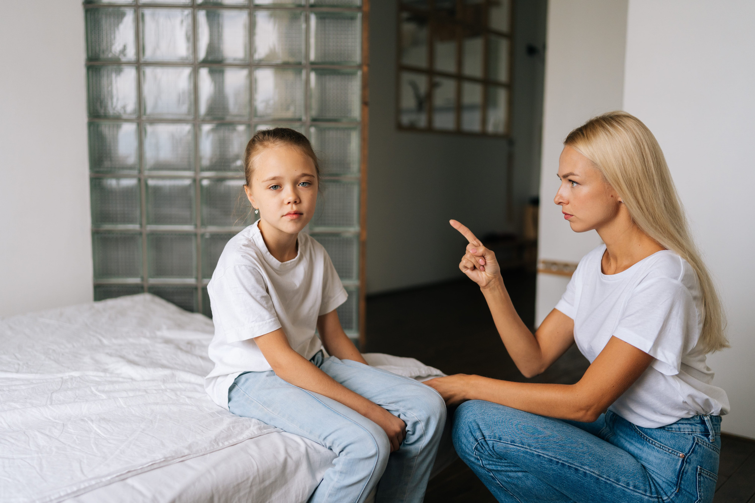 Aggressive young mom scolding, raising voice, scream and pointing fingers at stubborn difficult little child daughter sad looking at camera. Concept of mother-daughter problem in preteen years.