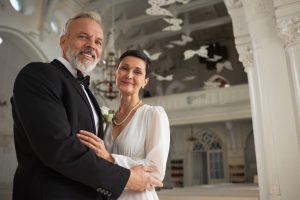 Waist up portrait of happy senior bride and groom looking at camera in church with smiles after wedding ceremony, copy space
