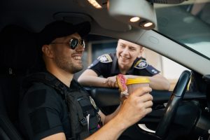 Smiling patrol police officers diverse team sitting in car having coffee break time at work