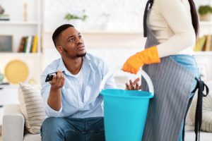 Lazy black man watching TV while his wife doing home cleanup, having fight with her, not wanting to help, indoors