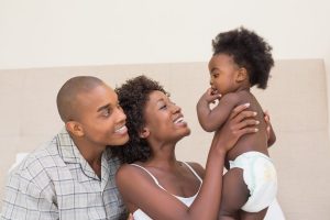 Happy couple on bed with baby daughter at home in the bedroom