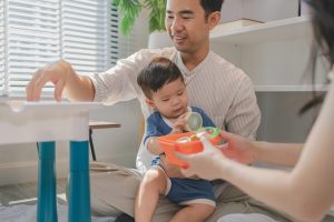 Happy young family playing with baby at home, parents engaging child with colorful toys and learning activities, showing love, care, early childhood development, and warm bonding moment together.