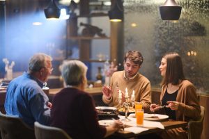 Four people sit at a table in a restaurant, enjoying iftar together during Ramadan. They share food and conversation while candles flicker in the background.