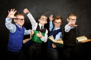 Group of smart boys in formal suits and spectacles standing with books by a blackboard.