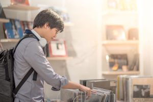 Young Asian man with headphones choosing disc in music shop, urban lifestyle concepts
