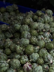 A close-up view of fresh artichokes piled up at an outdoor market stall, showcasing their vibrant green hues.
