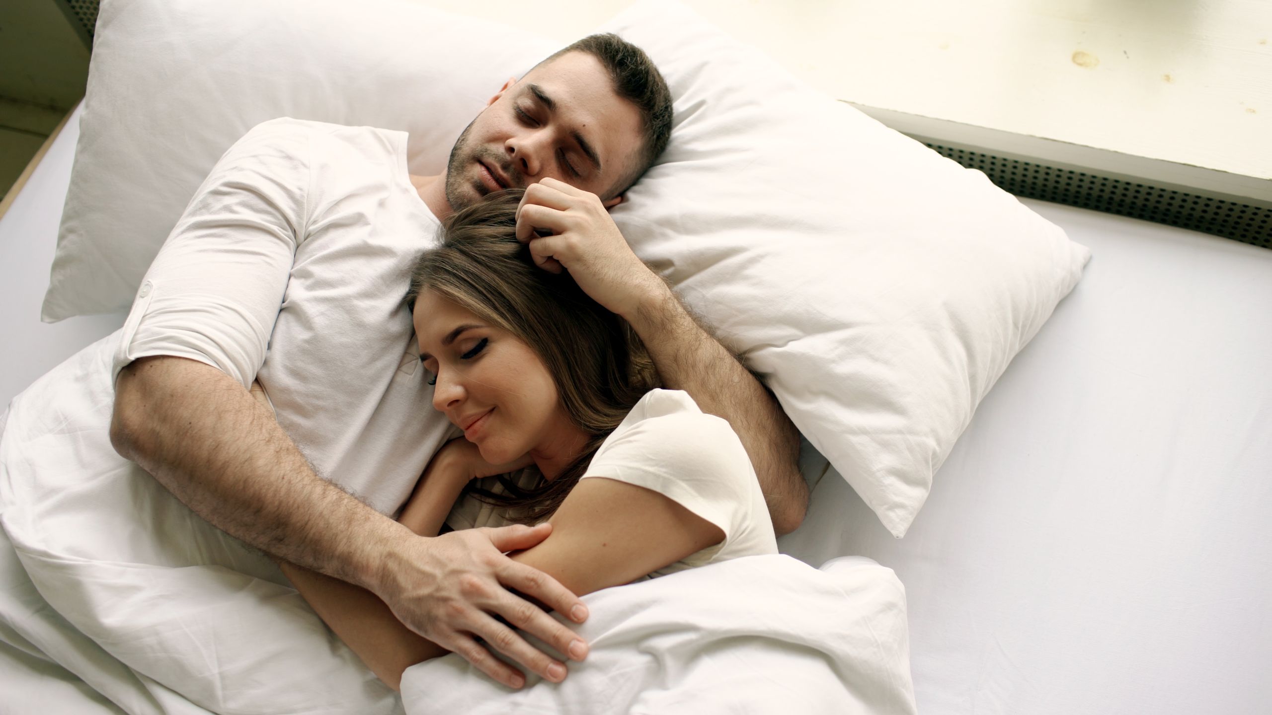 A couple peacefully embracing in a white bed, conveying warmth and intimacy.