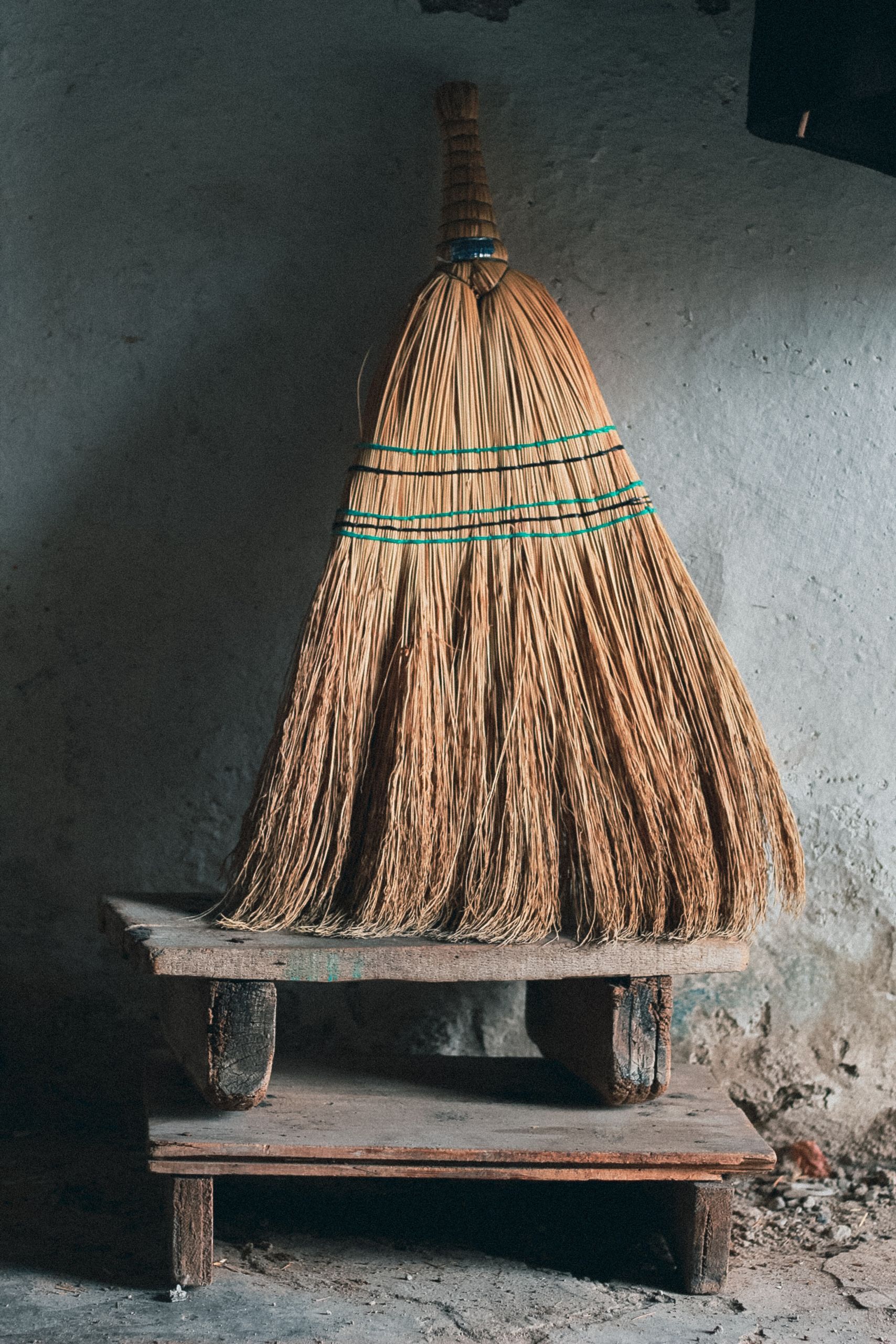 A detailed view of a straw broom placed on an old wooden step in a rural setting.