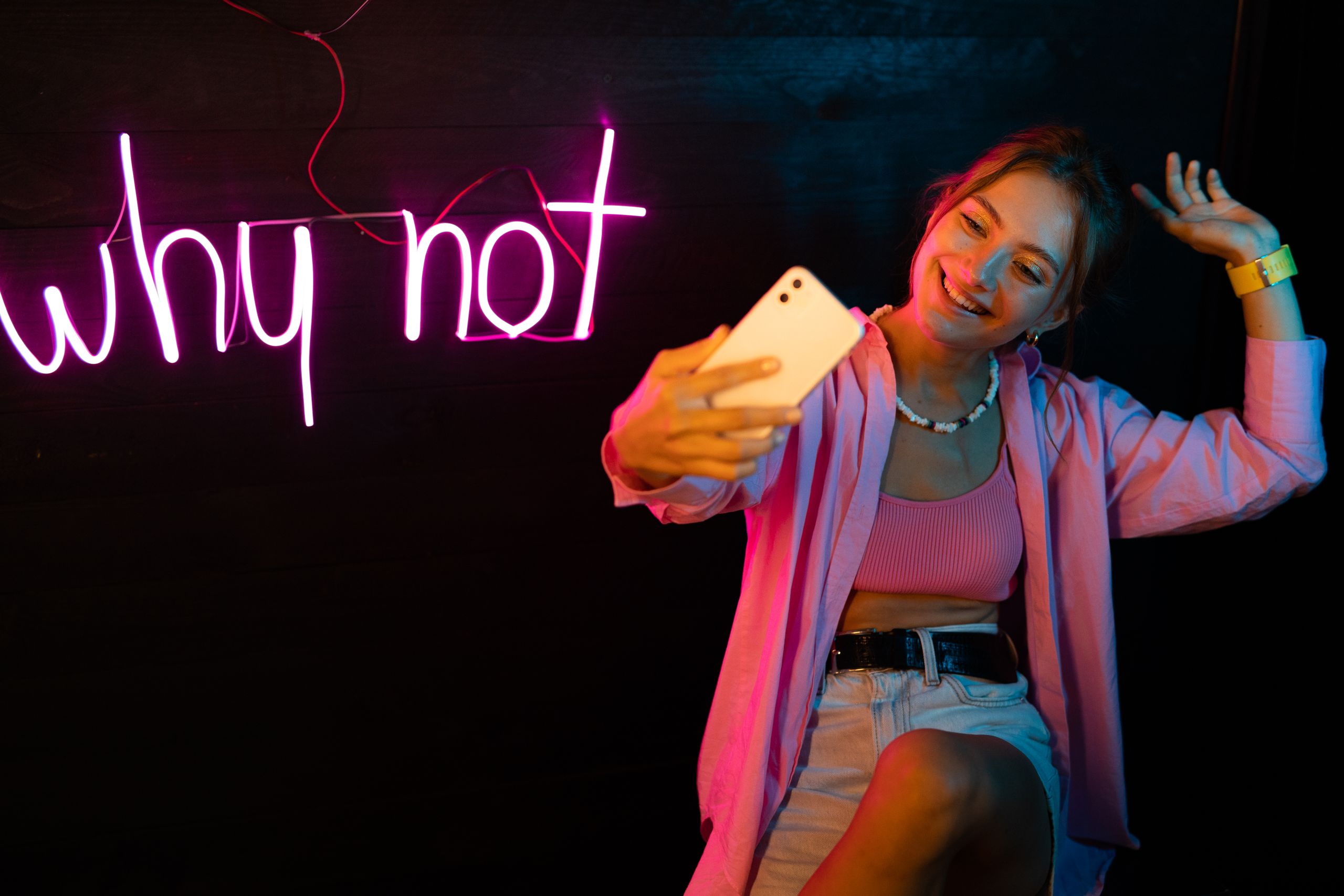 A fashionable young woman poses with neon lights and captures a selfie.