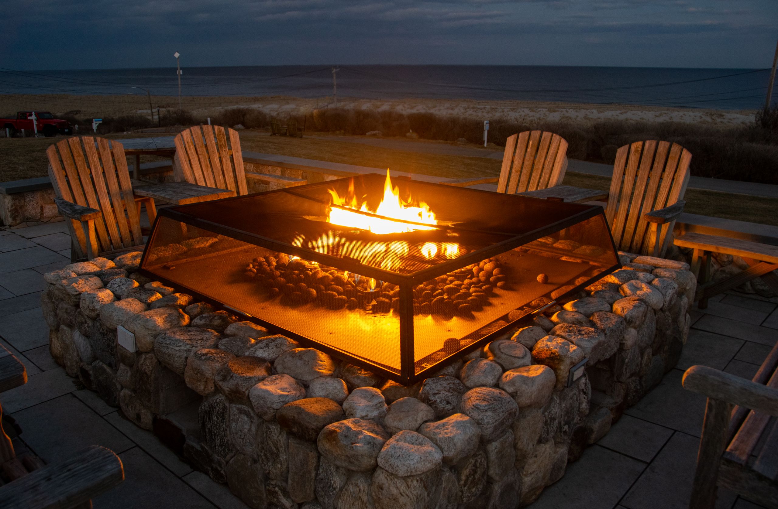 A glowing fire pit surrounded by Adirondack chairs near a beach in Orleans, Massachusetts, USA.