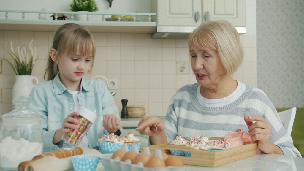 A grandmother and granddaughter decorating cupcakes together in a cozy kitchen.