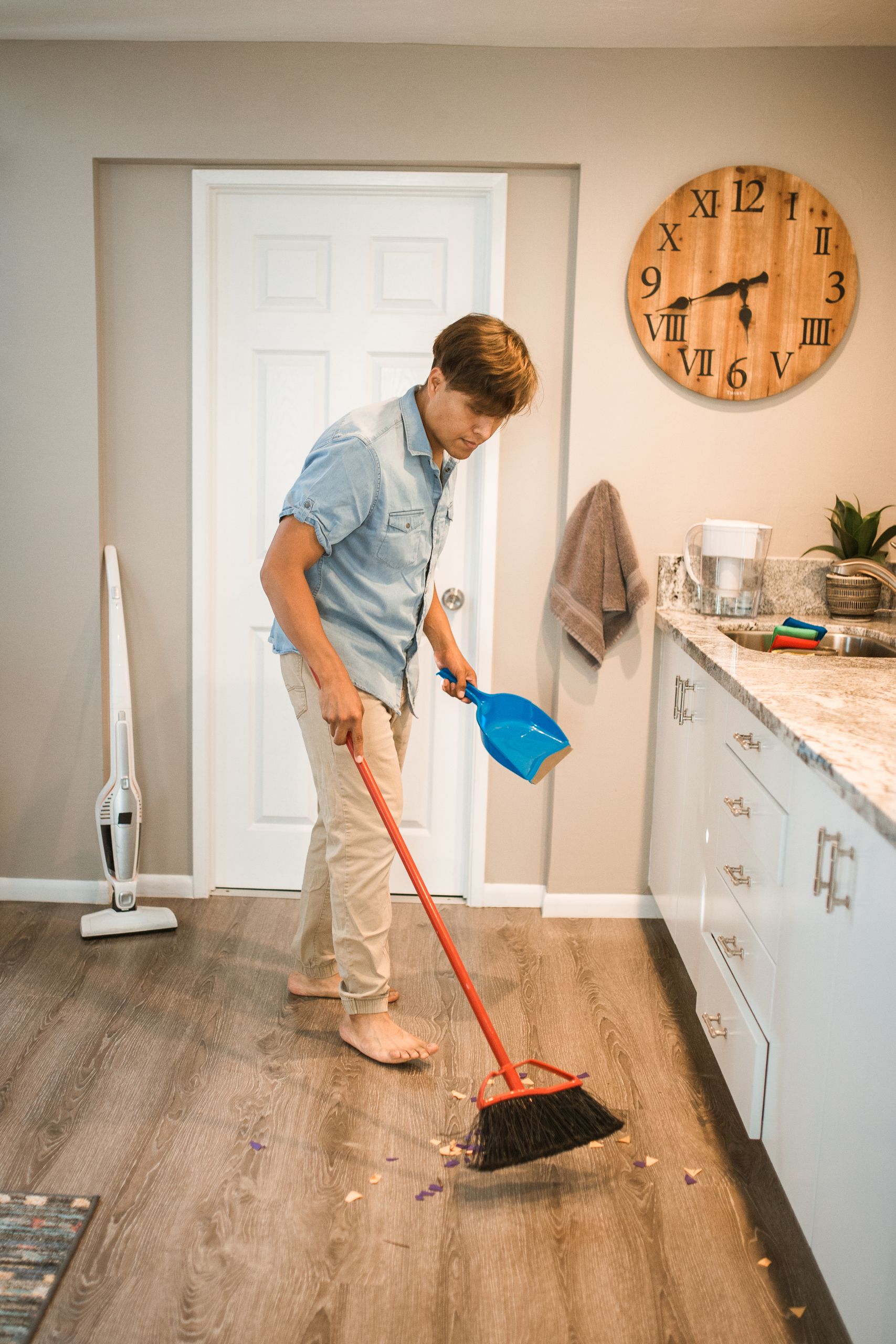 A man sweeping a kitchen floor with a broom and dustpan, performing a house chore.