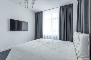 A modern bedroom featuring minimalist decor with a flat-screen TV and elegant curtains.