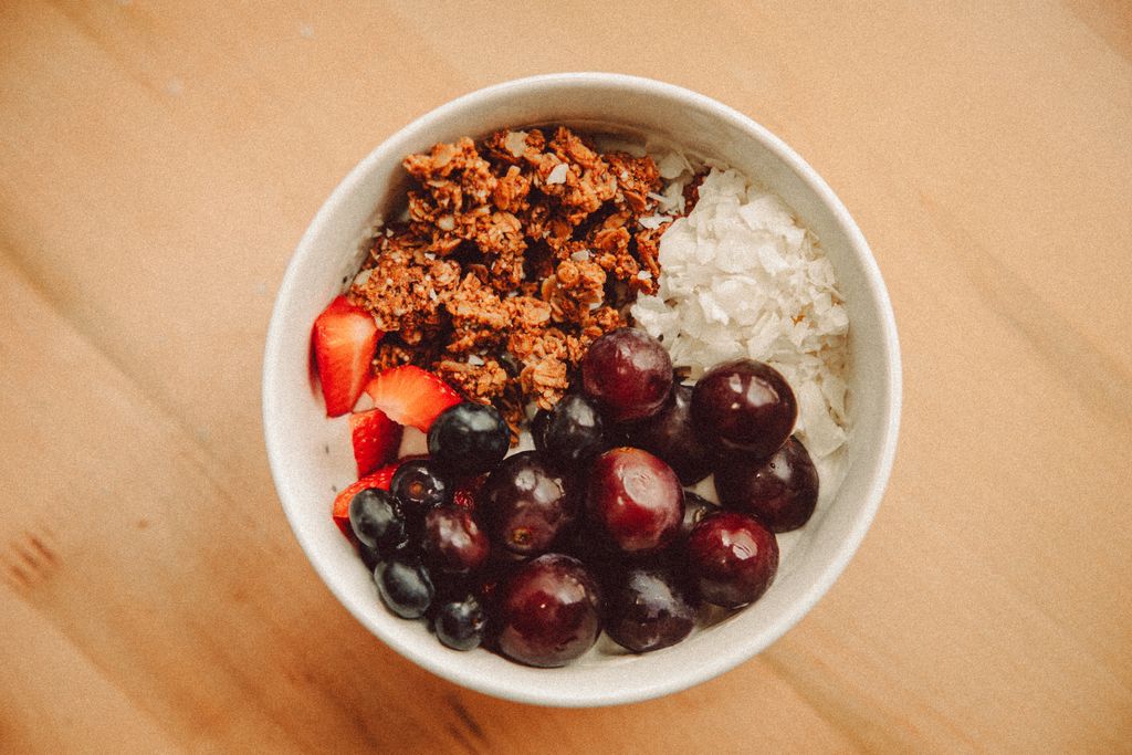 A nutritious breakfast bowl featuring grapes, strawberries, granola, and coconut flakes.