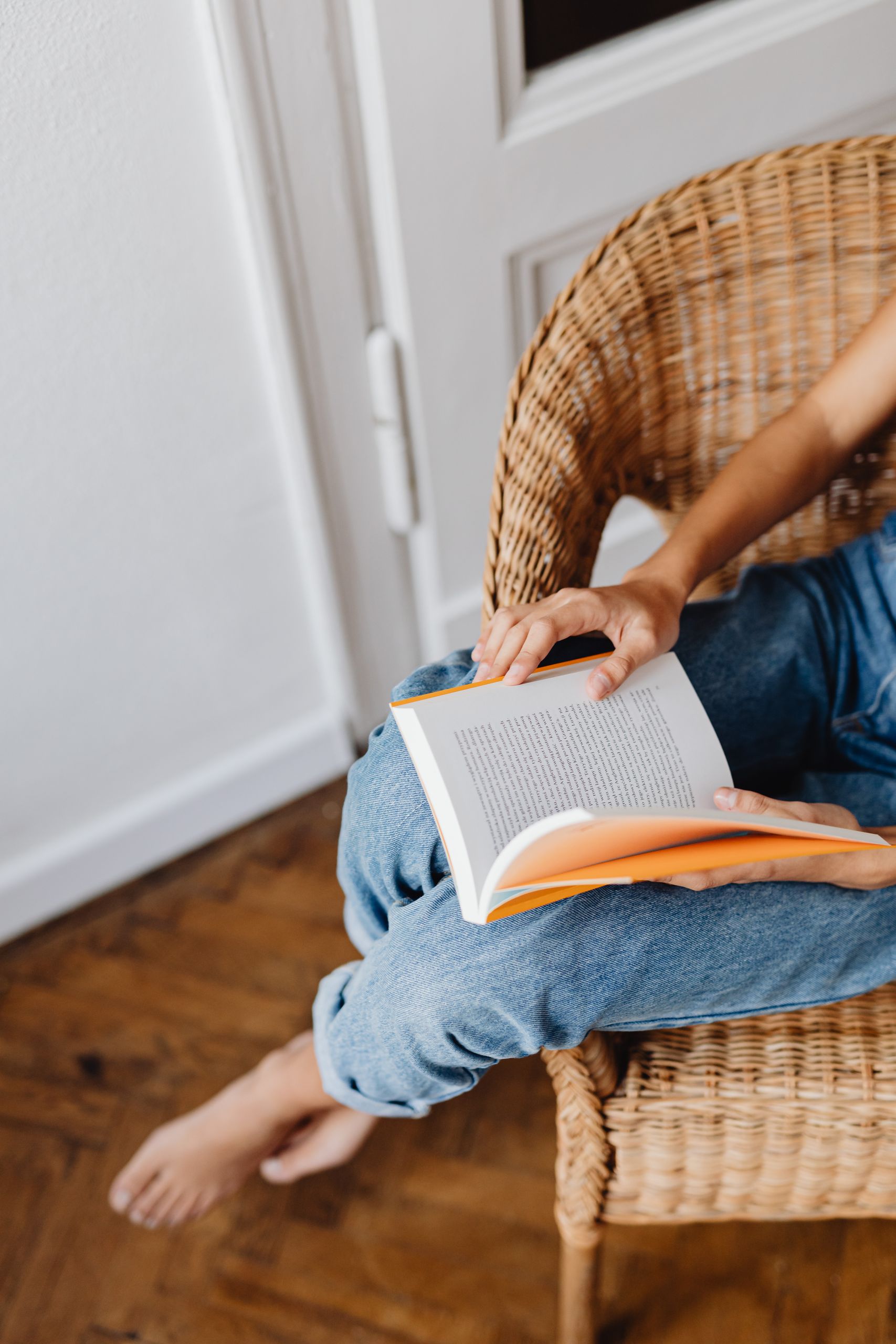 A person relaxing with a book in a comfortable wicker chair indoors.