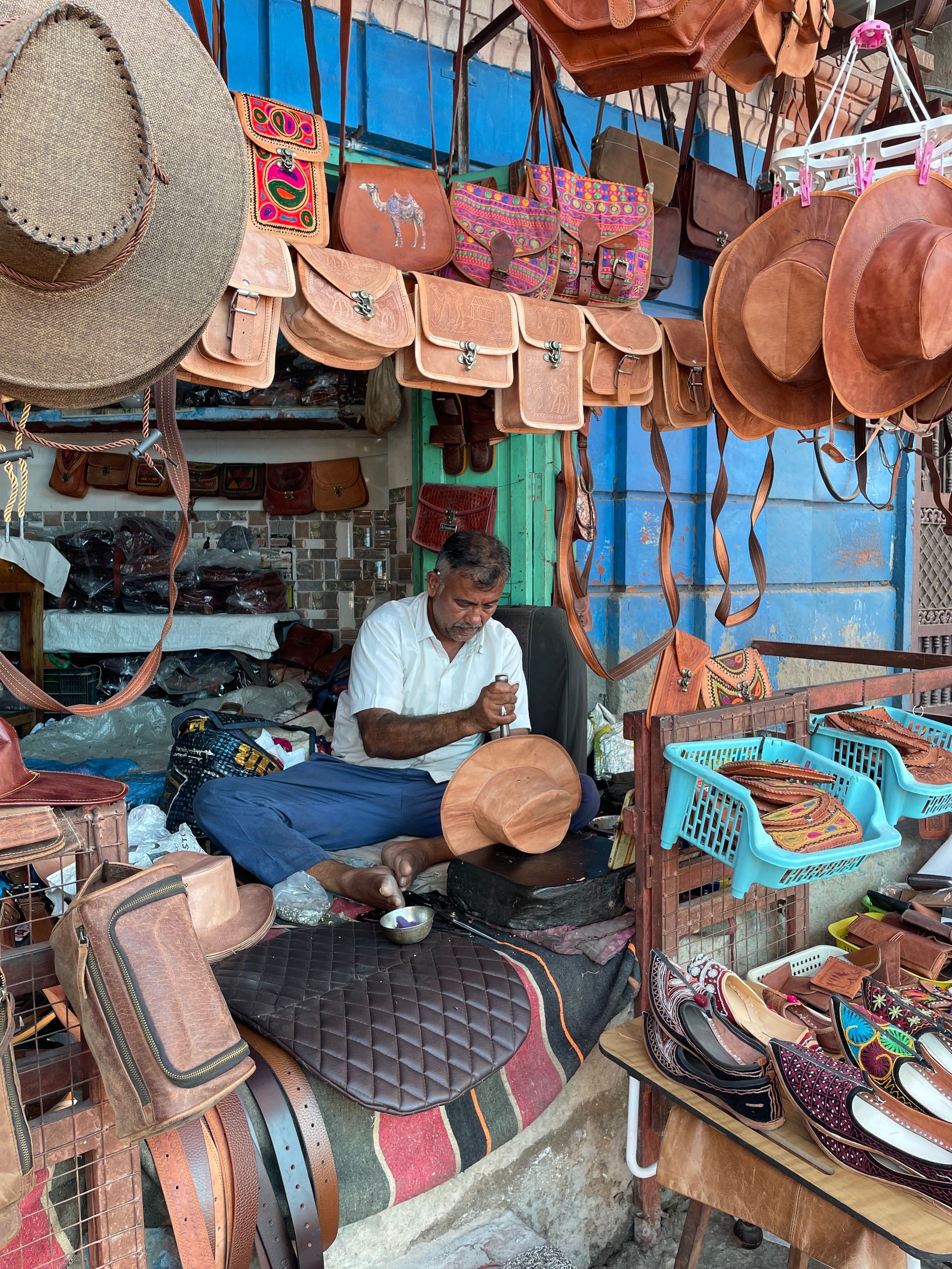A skilled artisan creating leather products in a bustling Jodhpur market.