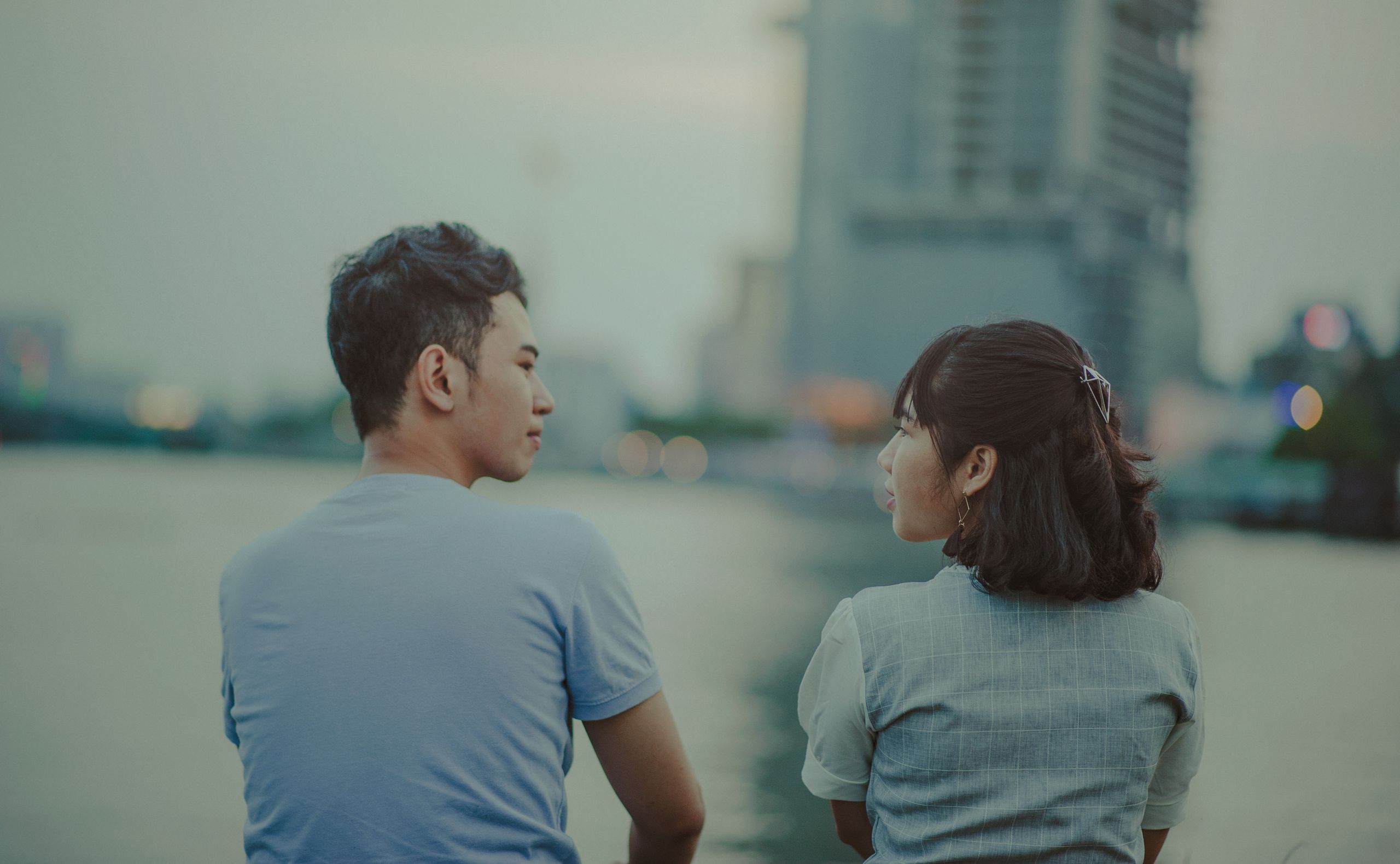 A young couple enjoys a peaceful moment by the riverside in an urban setting.