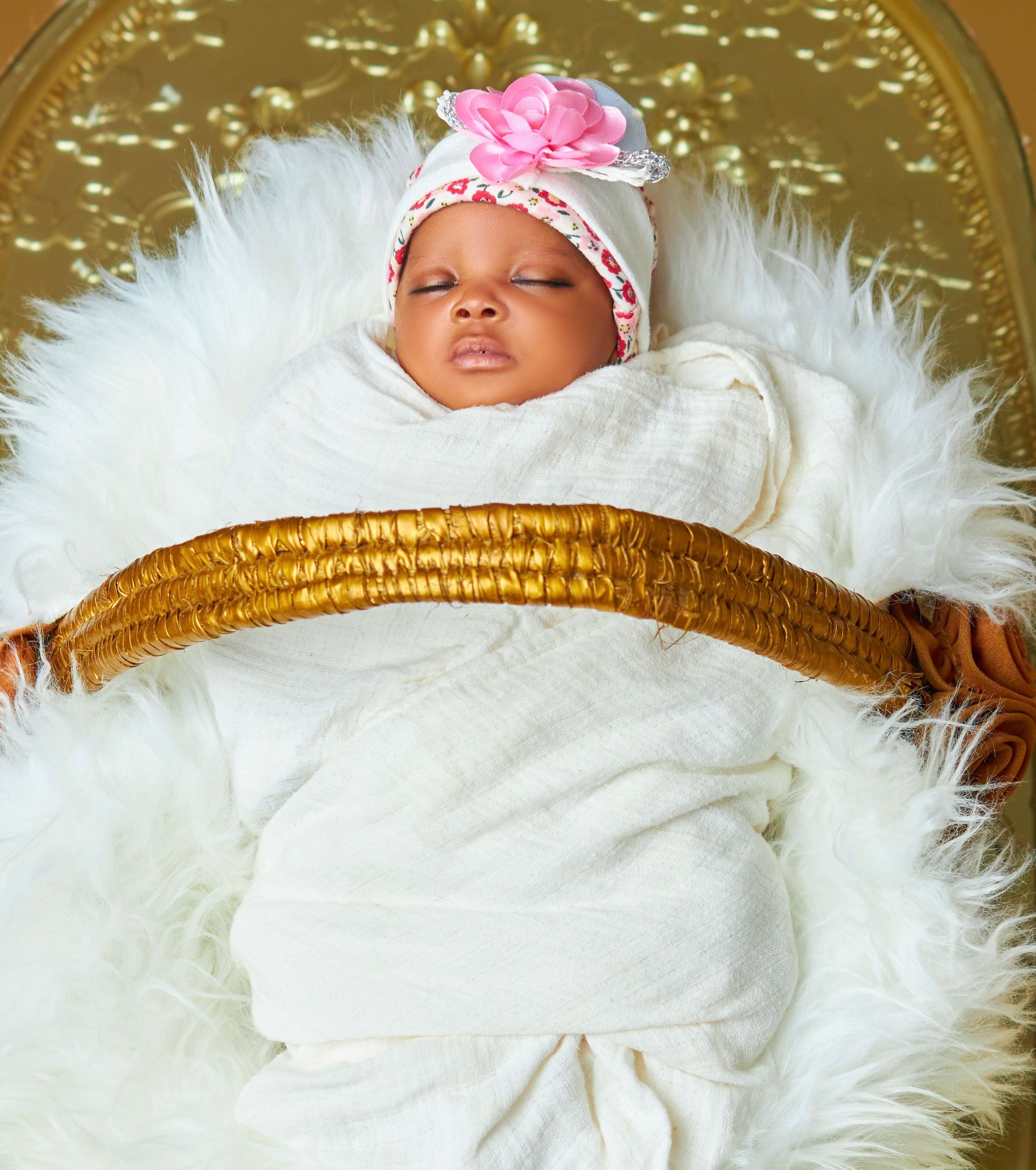 Adorable baby wrapped in a soft blanket sleeping peacefully in a golden basket.