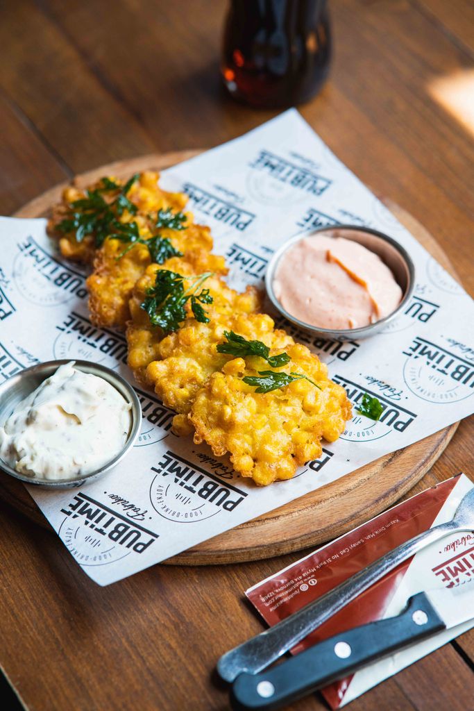 Appetizing corn fritters served with tangy dipping sauces on a wooden table, perfect for a pub-style meal.