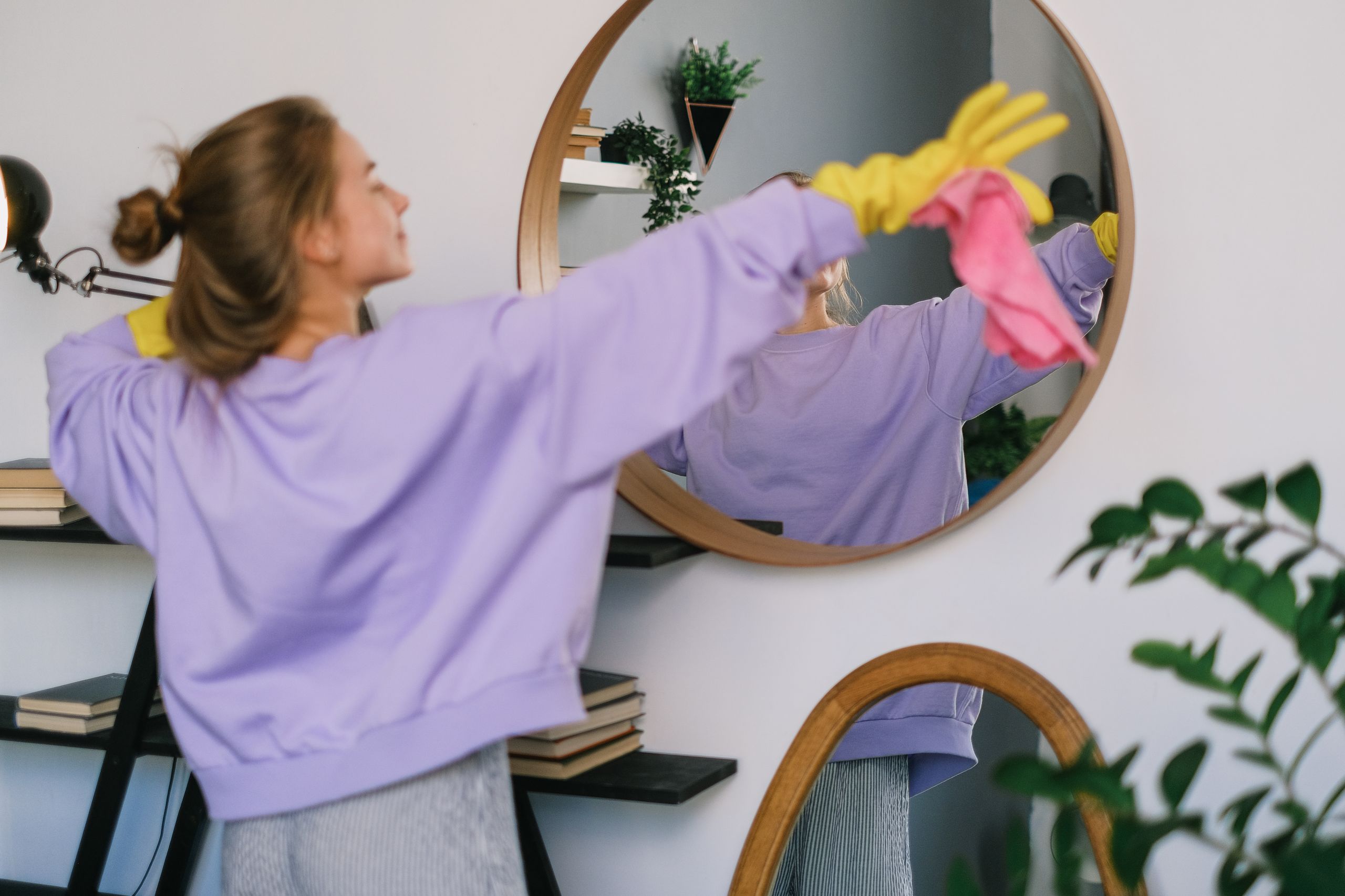 Back view of young female in casual clothes and yellow latex gloves dancing while cleaning light living room in daytime