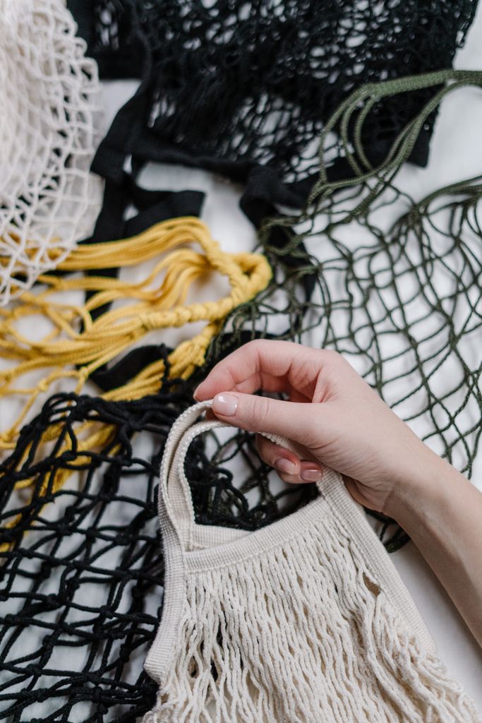 Close-up of a hand holding eco-friendly mesh bags in various colors emphasizing zero waste.