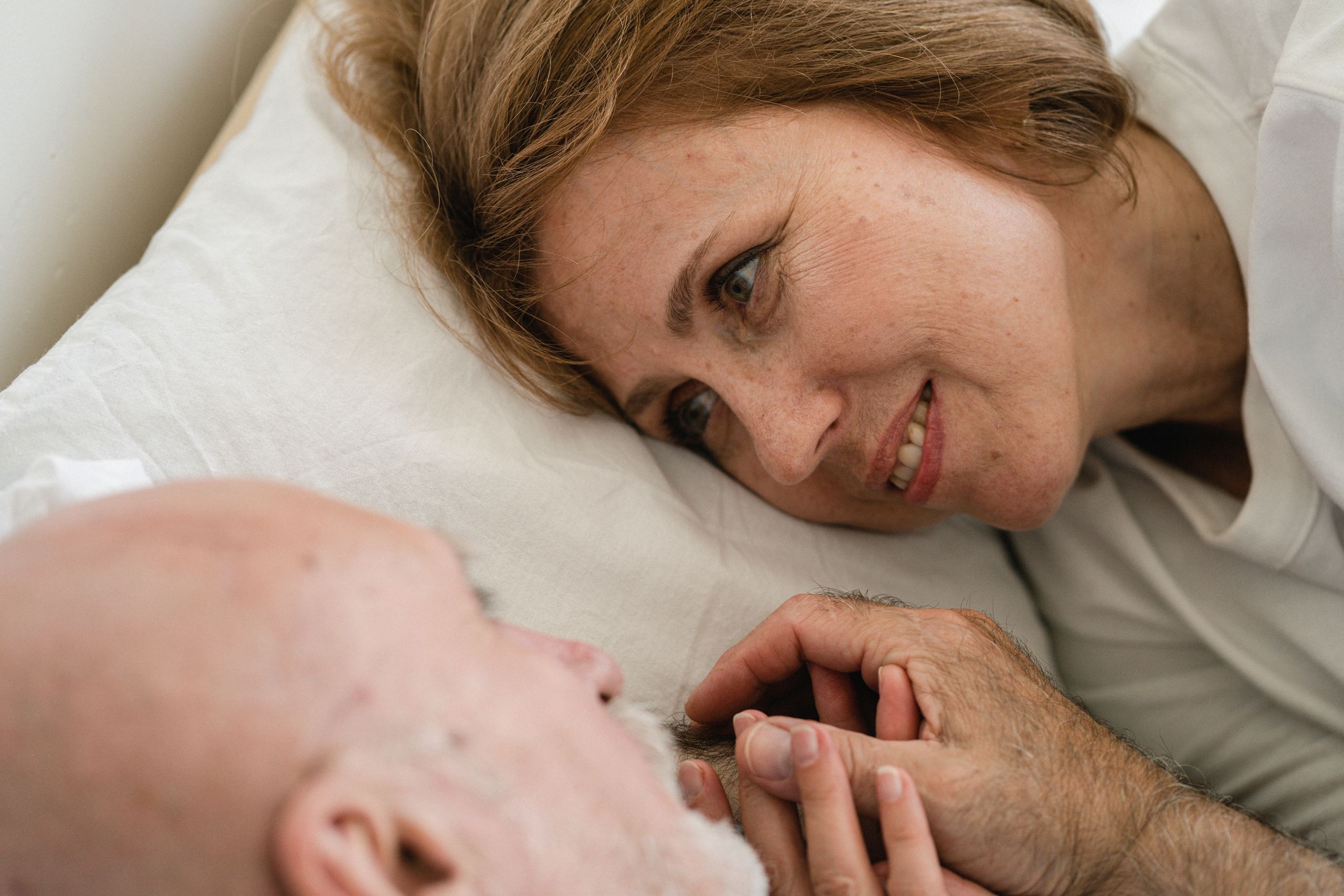 Close-up of a senior couple lovingly holding hands in bed, sharing a tender gaze.