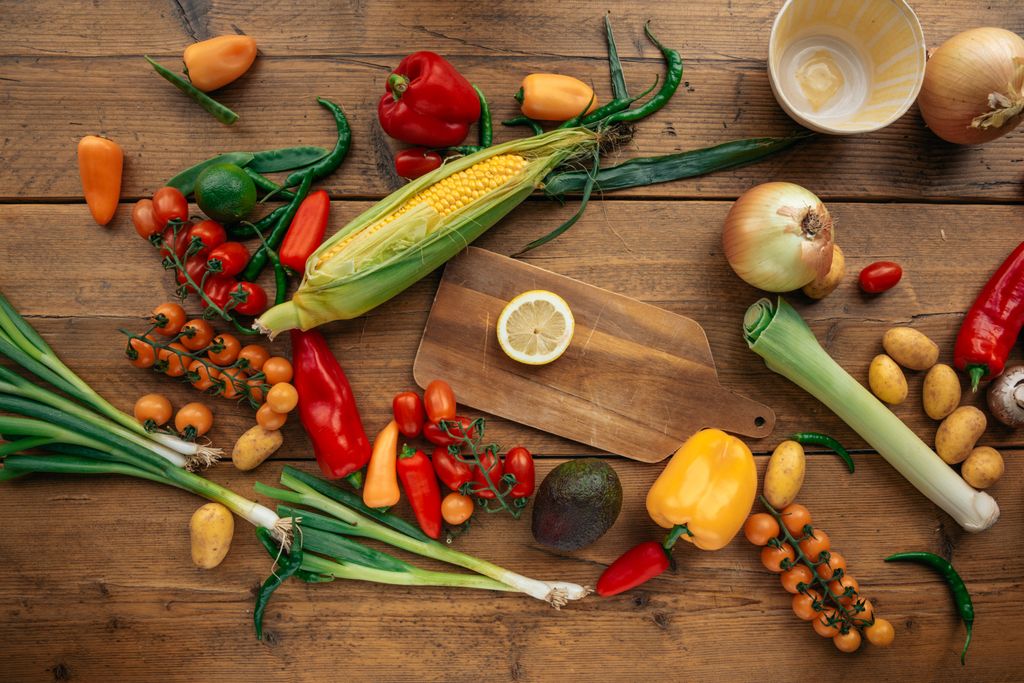 Colorful assortment of fresh vegetables and fruits arranged on a wooden table with cutting board.