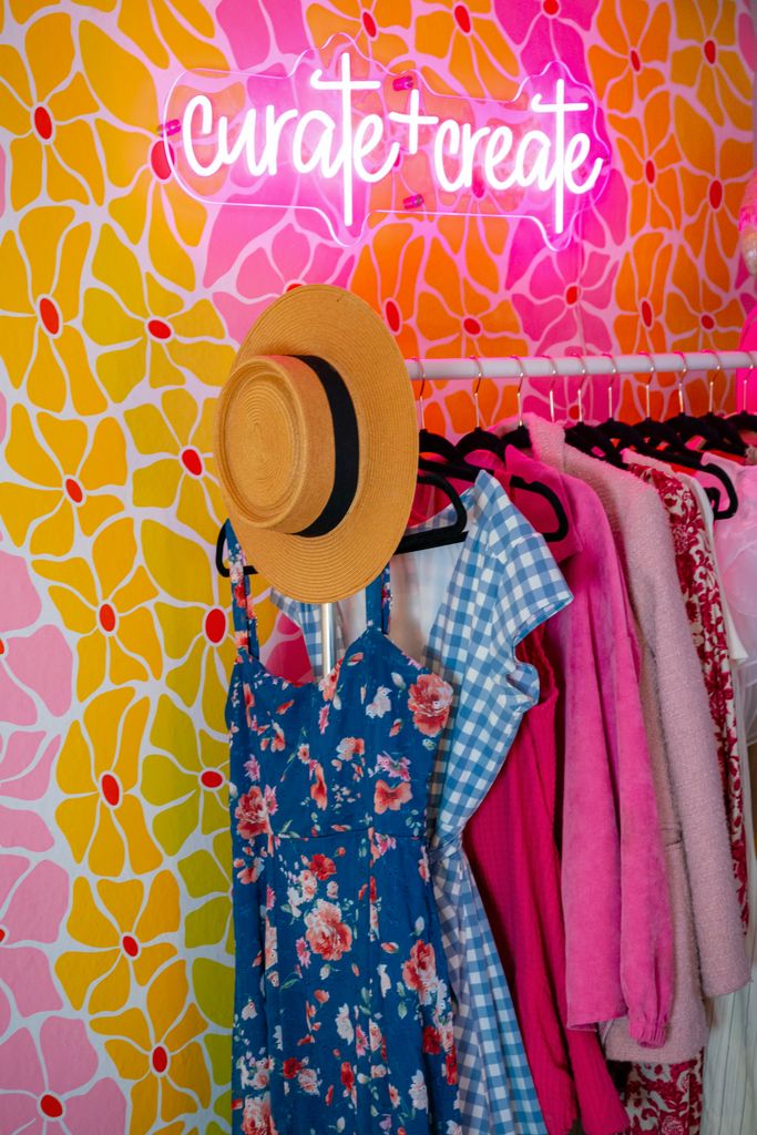Colorful clothes on a rack with neon sign 'curate + create'.