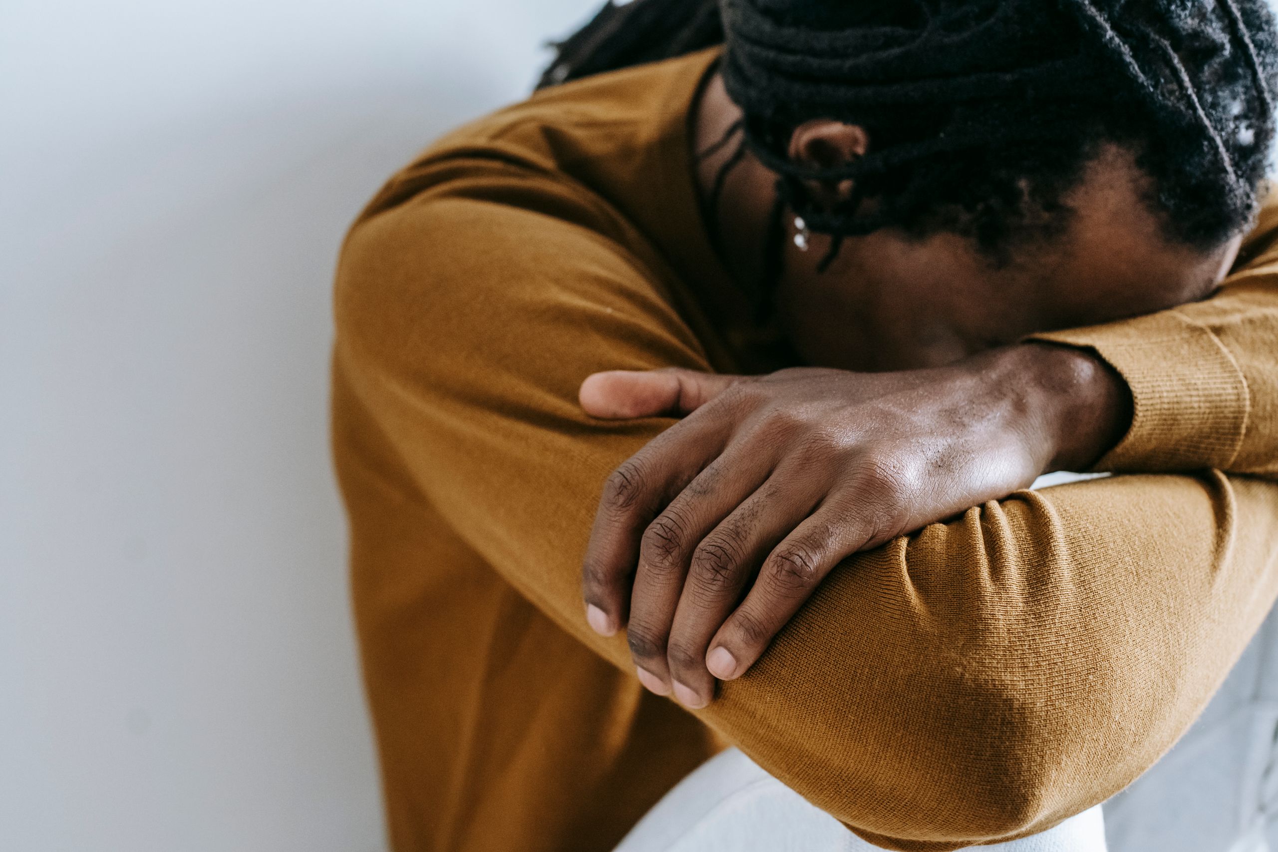 Crop anonymous unhappy African American male with dreadlocks in casual apparel leaning on hands in daytime