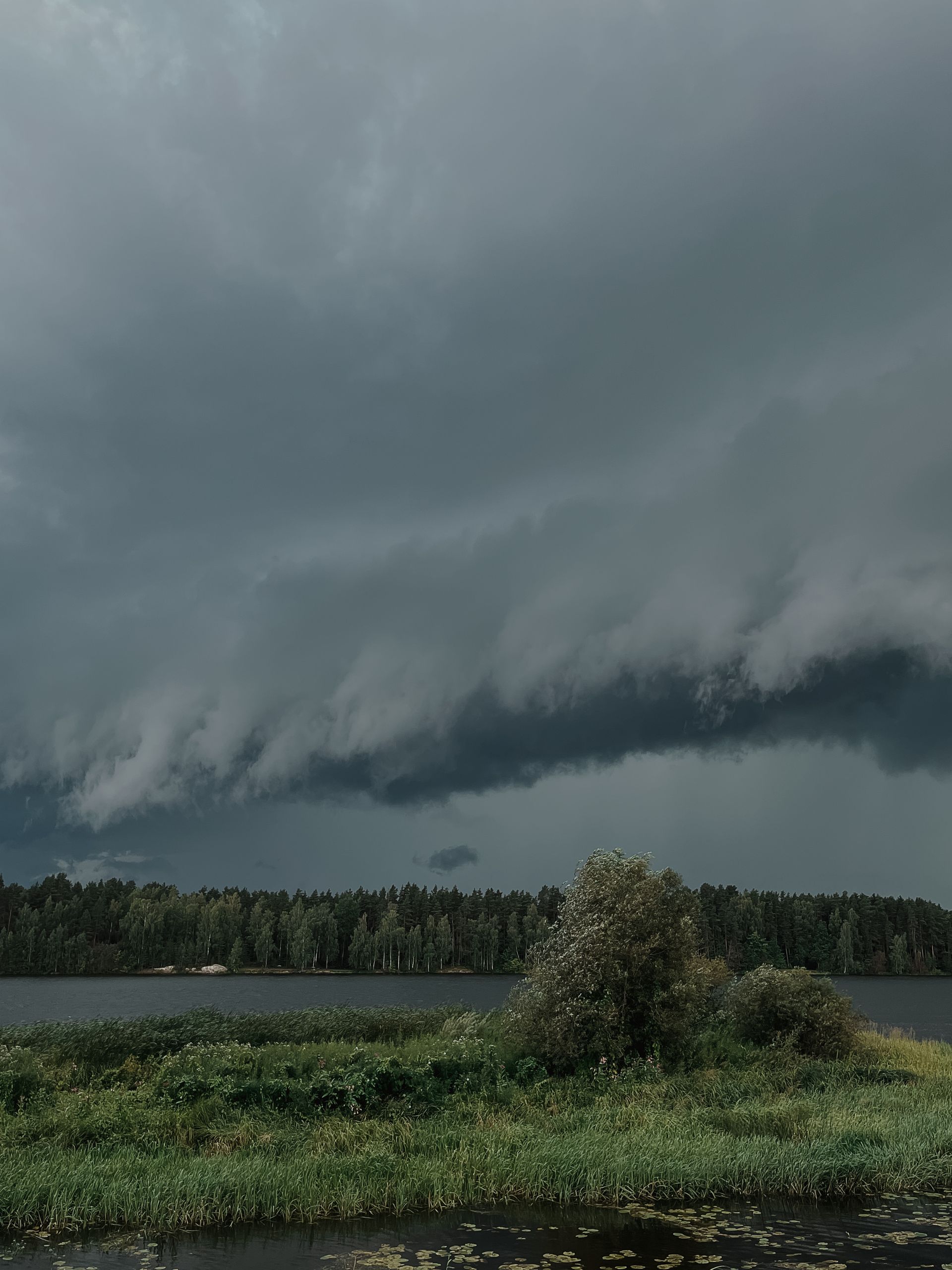 Dark storm clouds loom over a serene countryside lake and field, capturing the essence of nature's power.
